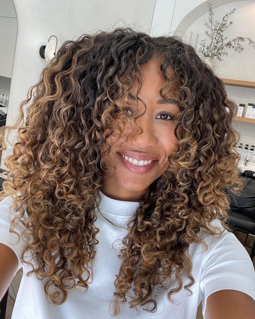 caramel highlights on curly hair with curtain bangs